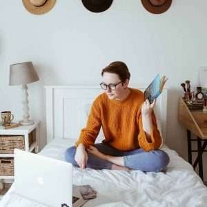 a cozy scene of a woman lounging in her bed and looking intently at her laptop.